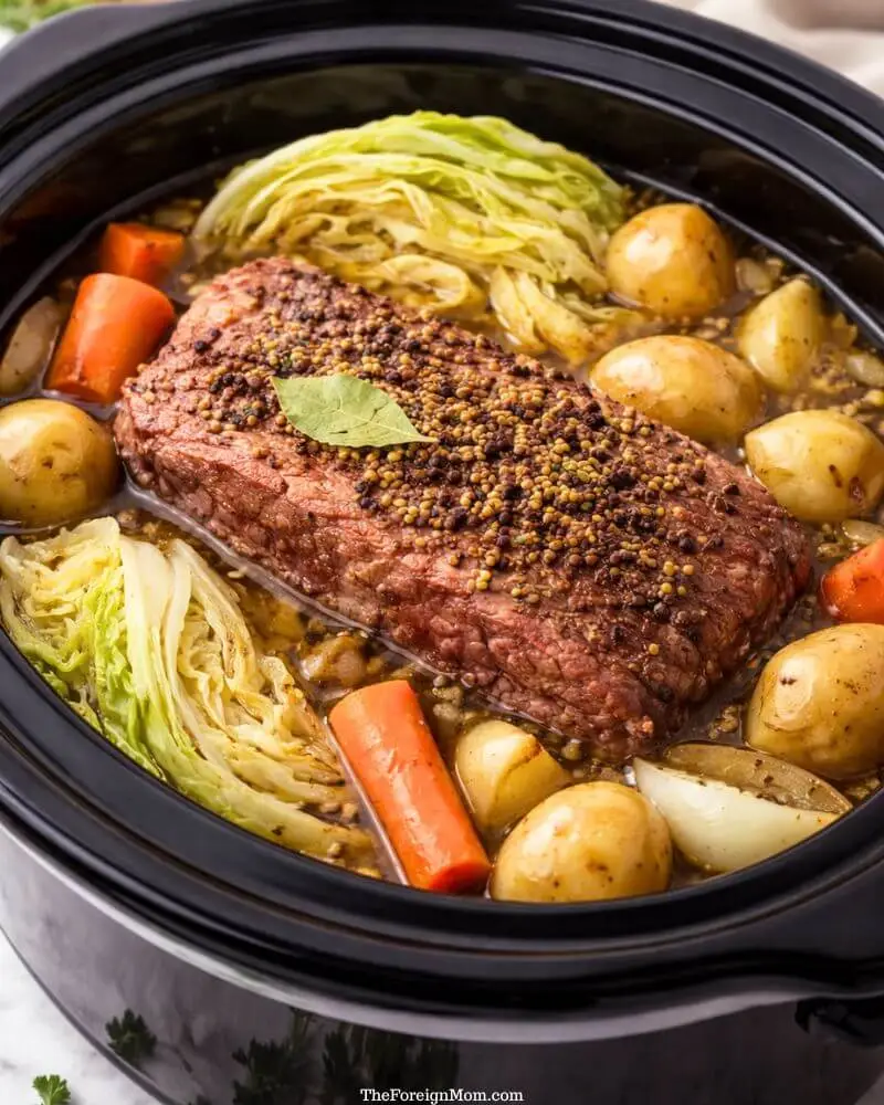 Corned beef brisket with cabbage, carrots, and potatoes cooking in a slow cooker crockpot.