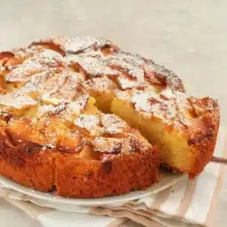 German apple streusel cake dusted with powdered sugar, sliced and displayed on a plate, soft apple-filled center and golden brown edges.
