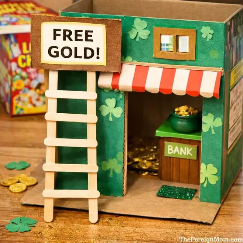 Cardboard leprechaun bank trap with a ladder, free gold sign, shamrock decorations, and gold coins for St. Patrick’s Day.