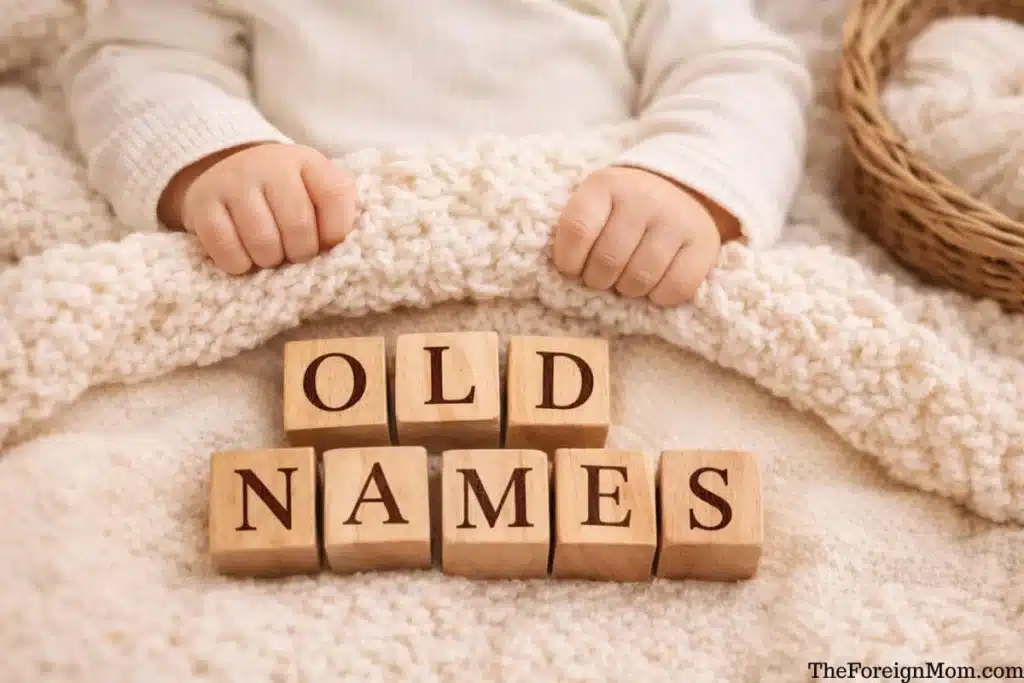 Baby hands holding a soft blanket with wooden blocks spelling old names for a vintage baby name list.