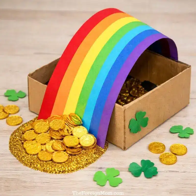Rainbow leprechaun trap made from a cardboard box filled with gold coins, a colorful rainbow path, and shamrock decorations for St. Patrick’s Day.