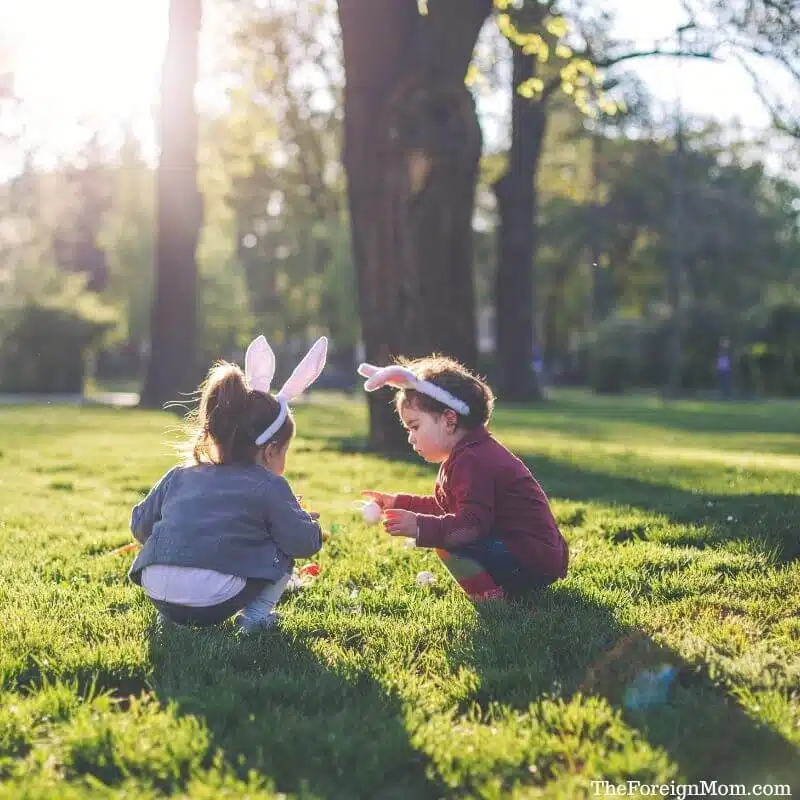 Two young kids wearing bunny ears during an Easter egg hunt with non-candy egg fillers in a sunny park.