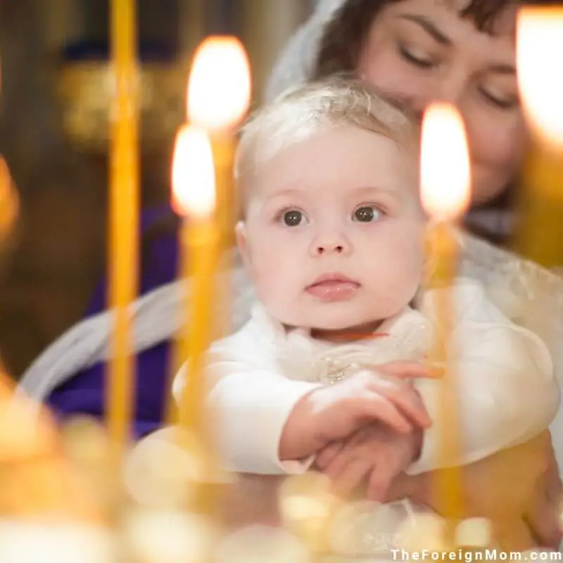 Baby looking on with wonder during a quiet faith-filled moment, held close and surrounded by candlelight.