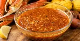 Bowl of homemade Juicy Crab sauce copycat recipe made with garlic butter, Cajun seasoning, and Old Bay seasoning served with crab legs and seafood boil ingredients.
