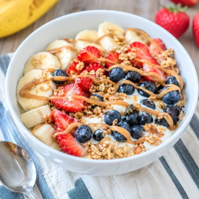 Banana split bowl with Greek yogurt, banana slices, strawberries, blueberries, granola, and peanut butter drizzle.