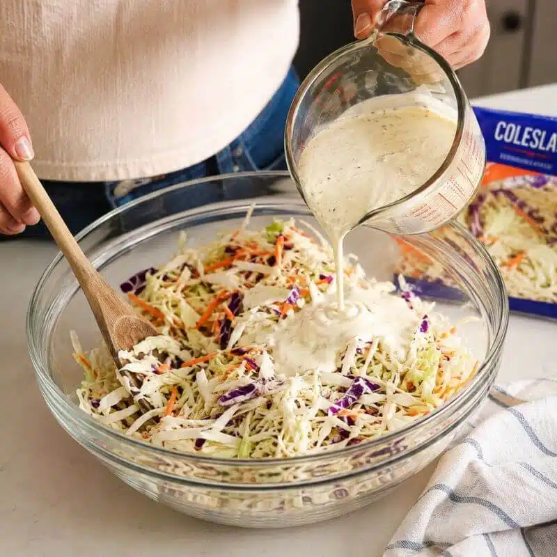 Shredded cabbage and carrots being tossed with creamy homemade coleslaw dressing.