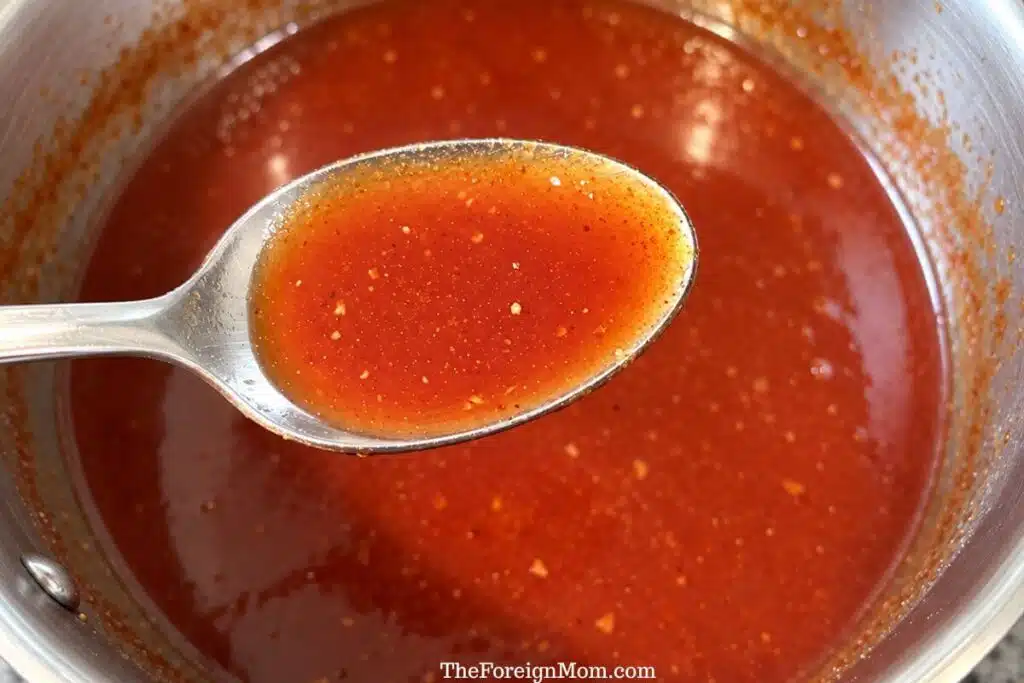 Spoonful of finished reddish-orange Country Sweet sauce held above a saucepan.