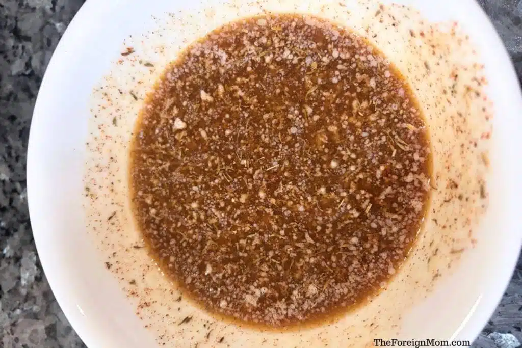 Melted butter mixed with dried herbs and spices in a white bowl.