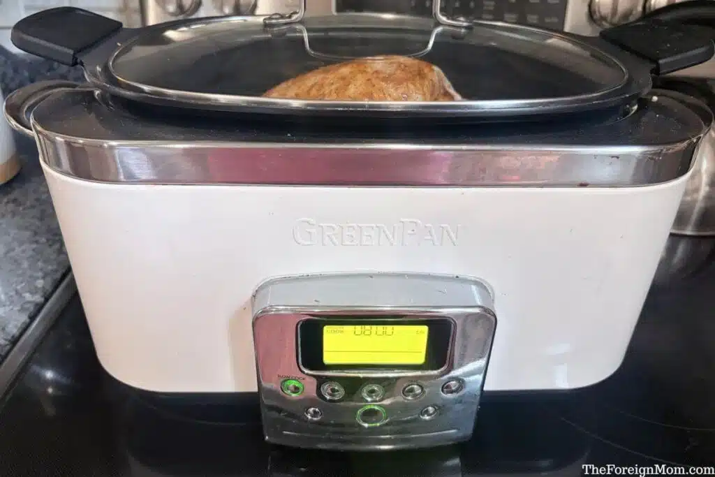 Covered slow cooker containing seasoned whole chicken, with the display set to low for eight hours.