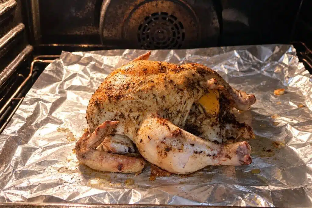 Lemon herb whole chicken with lightly browned skin on a foil-lined baking sheet inside the oven.