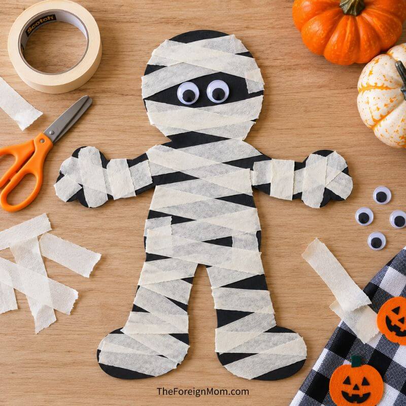 Finished black paper mummy craft with white masking tape strips and googly eyes.