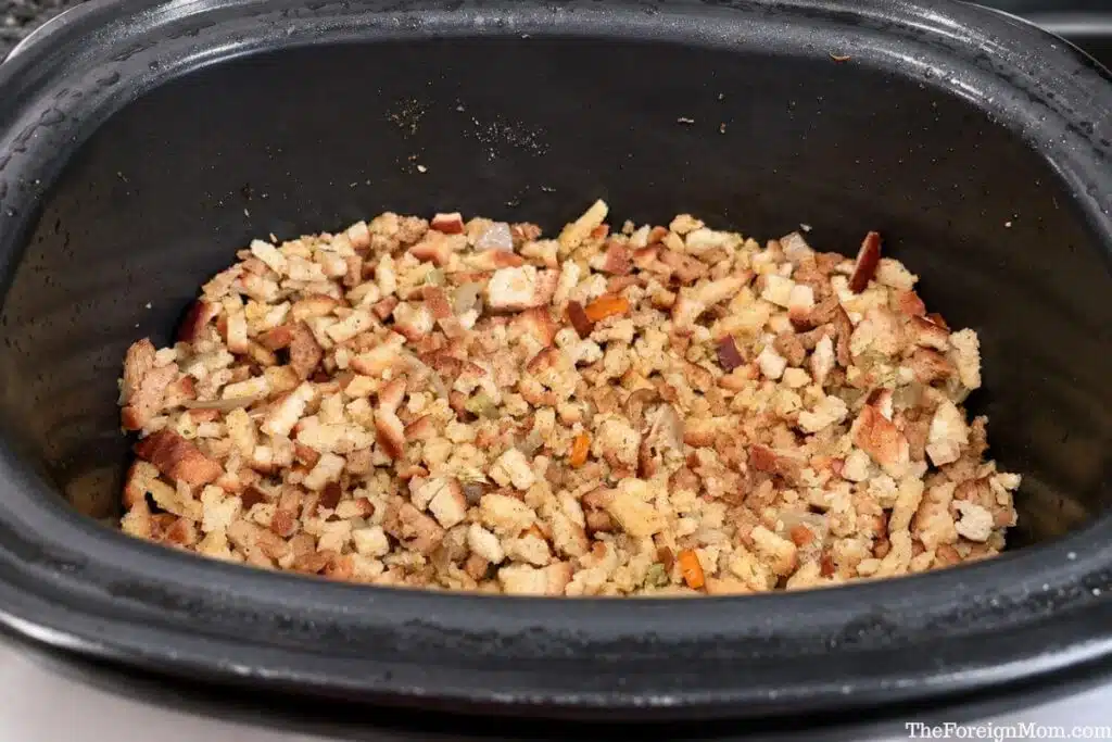 Bread stuffing mixed with carrots, celery, and onion in a black slow cooker.