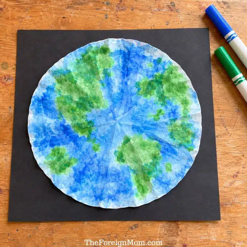 Round coffee filter colored blue and green to resemble Earth, mounted on black construction paper.