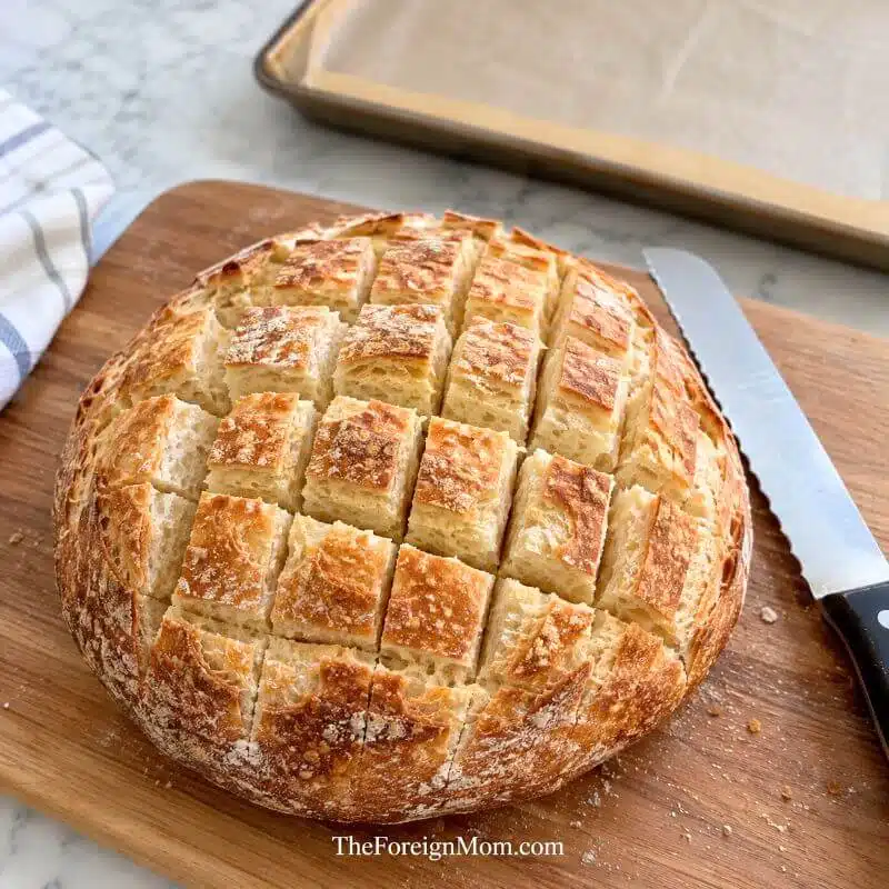 Round sourdough loaf cut into a crosshatch pattern on a wooden cutting board, ready to be filled with creamy Brie cheese and cranberry sauce for cranberry Brie pull apart bread.