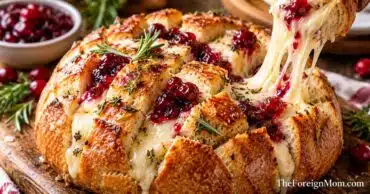 Golden brown cranberry brie pull apart bread filled with creamy melted Brie cheese, tart cranberry sauce, and fresh rosemary on a wooden serving board.