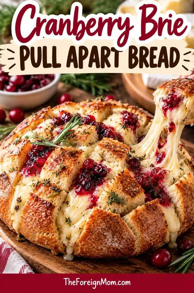 Golden brown round pull apart bread stuffed with gooey brie and cranberry sauce, with one piece lifted to show the melted cheese.