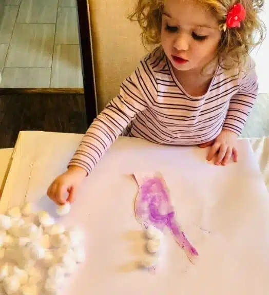 Toddler putting cottons balls on v-sign.
