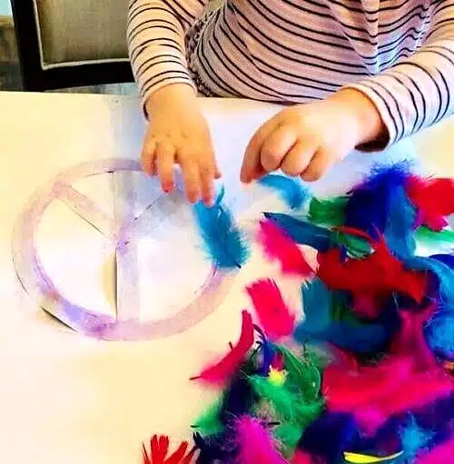 Craft of traditional peace sign with purple glue and colorful feathers